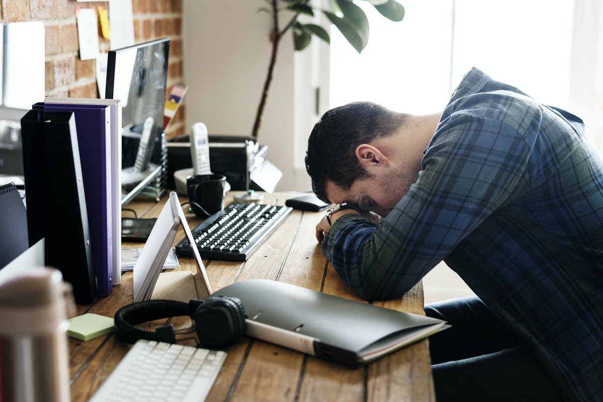 A man rests his head on his desk in the middle of working.