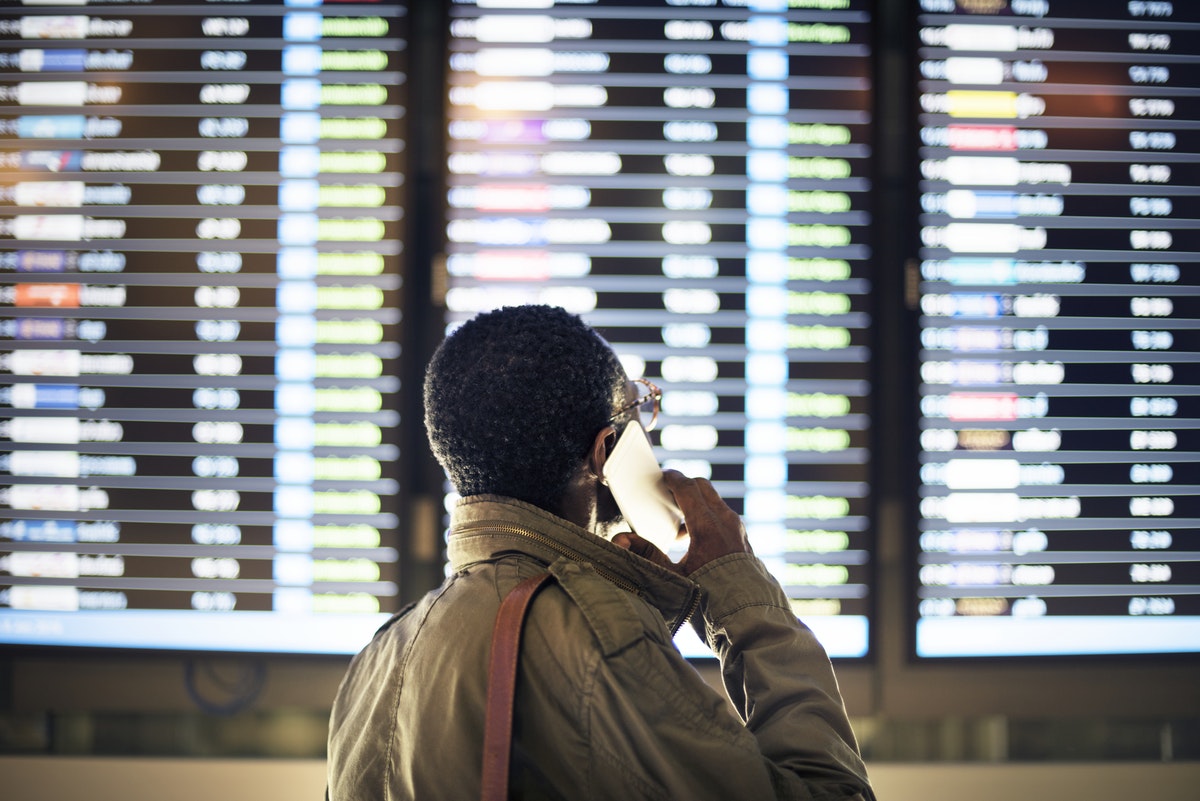 A man reads the arrivals and departures board at the airport while holding his phone to his ear, taking a call.