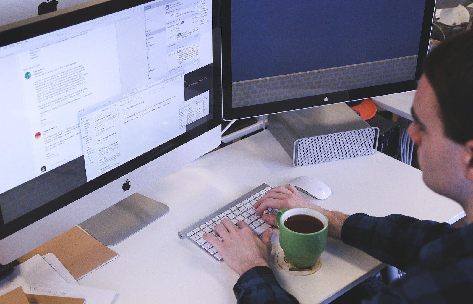 A man works on his computer with screen space to spare, one of the benefits of dual monitors.