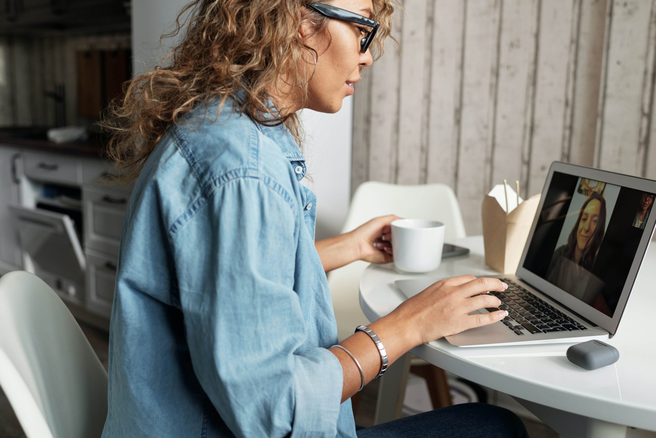 A woman drinks coffee and video chats with a friend while socializing online.