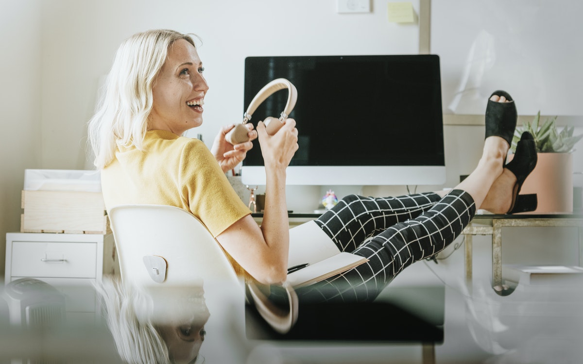 A woman prepares to put on her wireless headphones as she relaxes at her desk before a video conference.