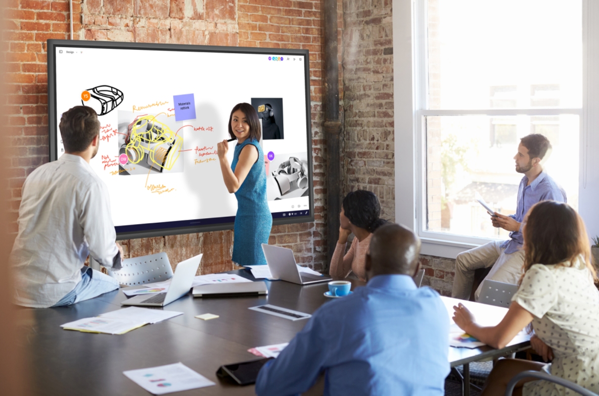 A woman draws on a interactive whiteboard during a team meeting after preparing with a conference room checklist.