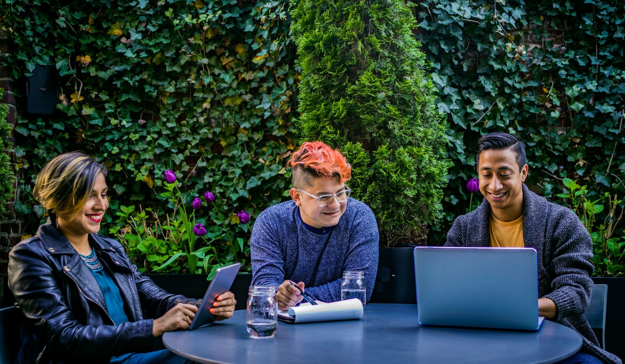 Three coworkers sit outside and review the features of their remote collaboration software.