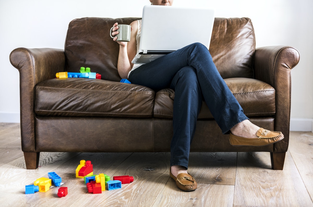 A woman sits on a couch with building blocks scattered at her feet as she works from home.