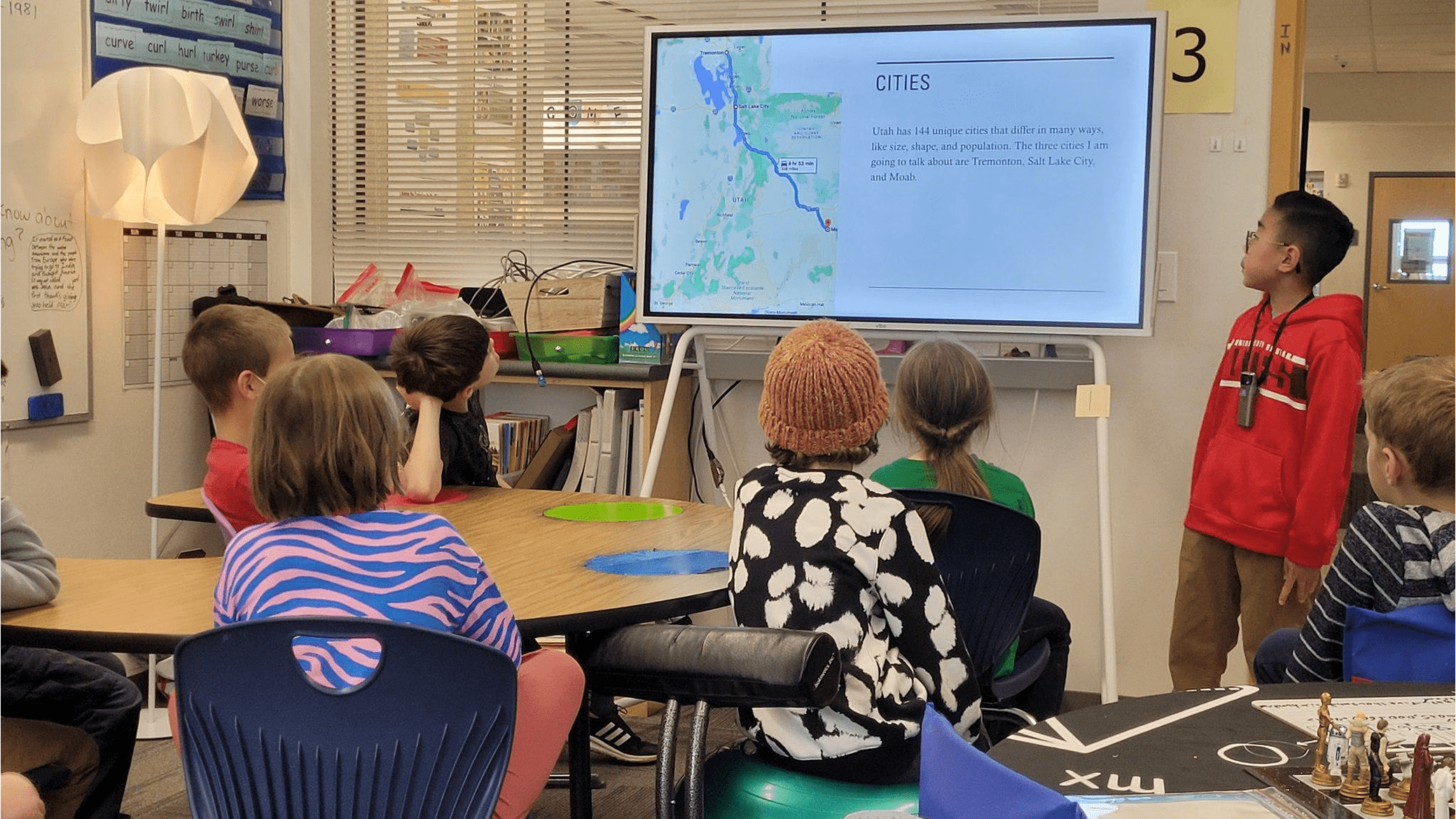 Confident student presenting project to classmates using smart whiteboard.